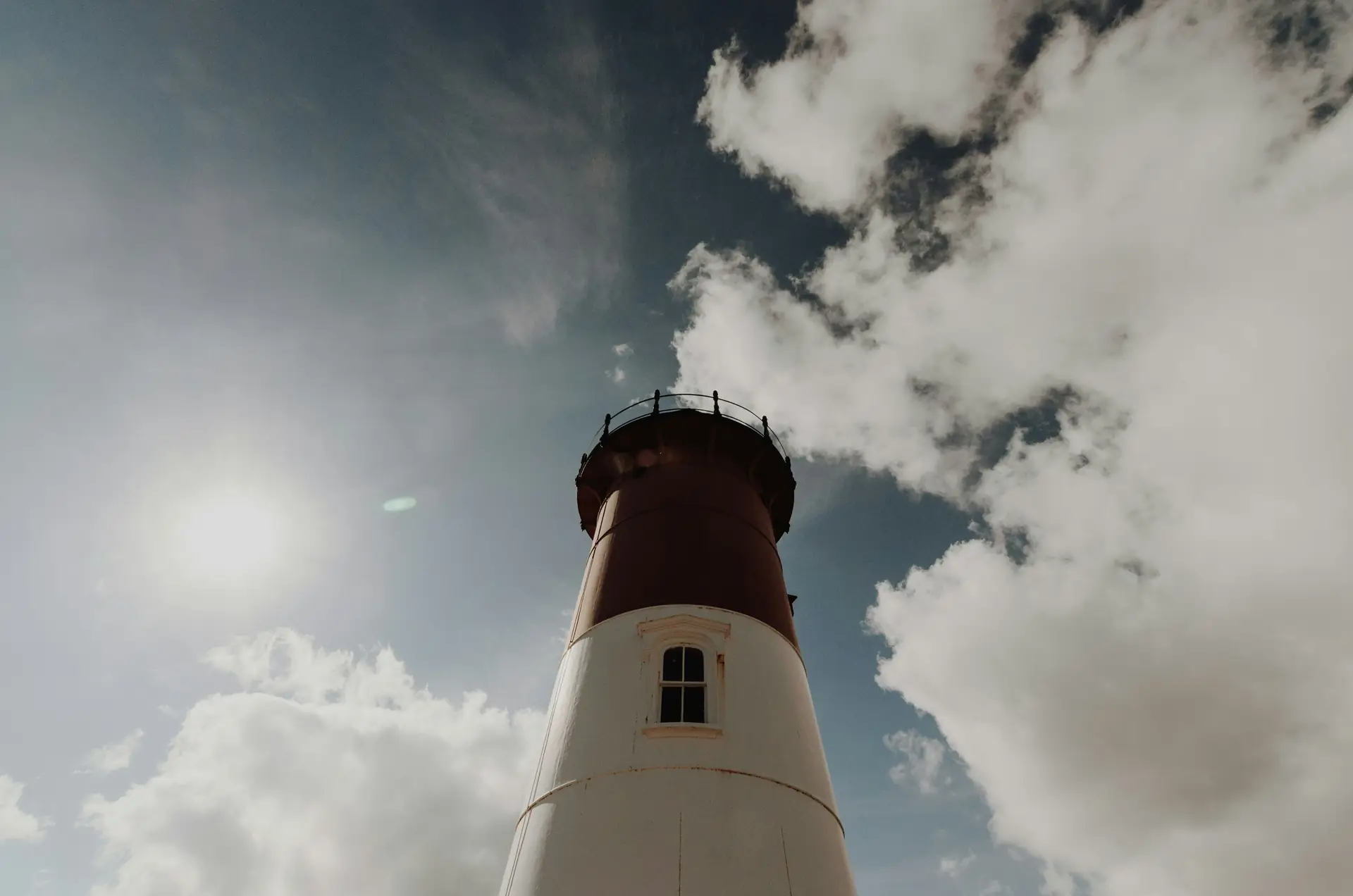 Nauset Light, a red and white Cape Cod lighthouse, beneath a partly cloudy blue sky